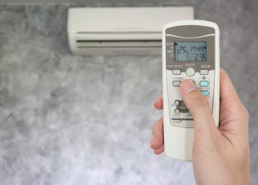 Hand holding remote in front of air conditioner.